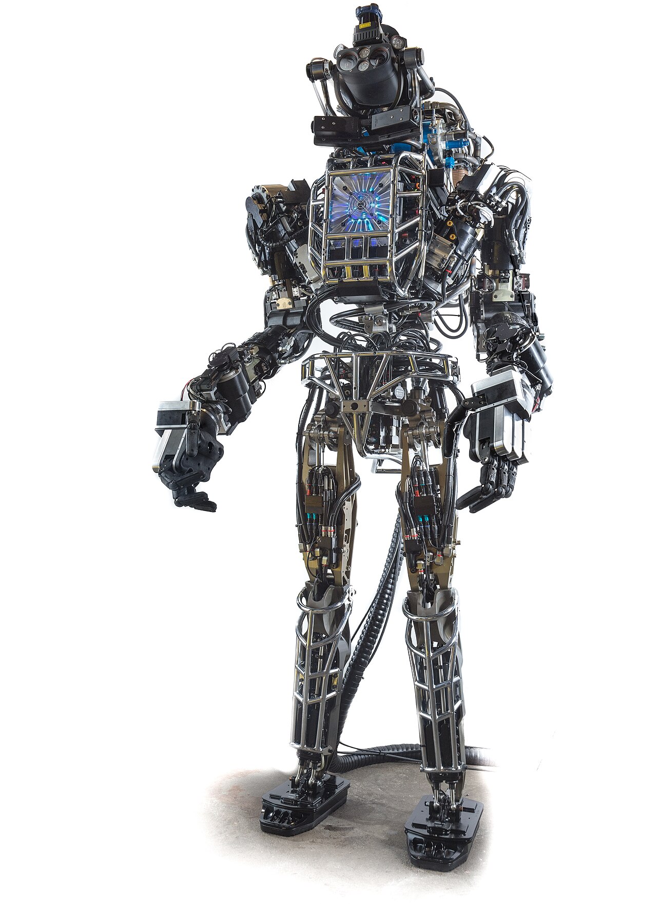 The 2013 DARPA Atlas humanoid robot stands facing forward with its exposed metal frame, hydraulic lines, and stereo camera head visible.